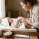 Parent drying a calm baby after a bath with coconut oil, oat powder, and ointment nearby