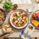 A colorful no-cook summer meal spread including Caprese salad, chickpea salad, and fresh fruit