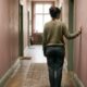 Person standing in a softly lit hallway with hand on wall, representing the quiet moment of recognizing a trauma response in yourself