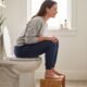 A woman using footstool positioned for proper toilet posture to relieve constipation