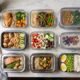 A variety of glass, plastic, and stainless steel meal prep containers filled with portioned meals