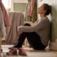 Woman sitting against a wall at home completely still with children's shoes in the background, representing the moment of collapse in a nervous breakdown